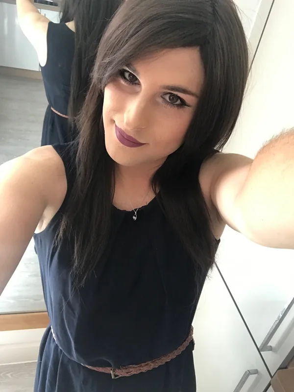 Portrait en selfie d'une personne aux cheveux noirs portant une robe bleu marine et un rouge à lèvres violet, regardant l'objectif.